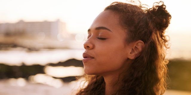Woman of color with eyes closed looking peaceful outside at sunset
