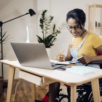 Black woman in a wheelchair working on a computer and with a notebook