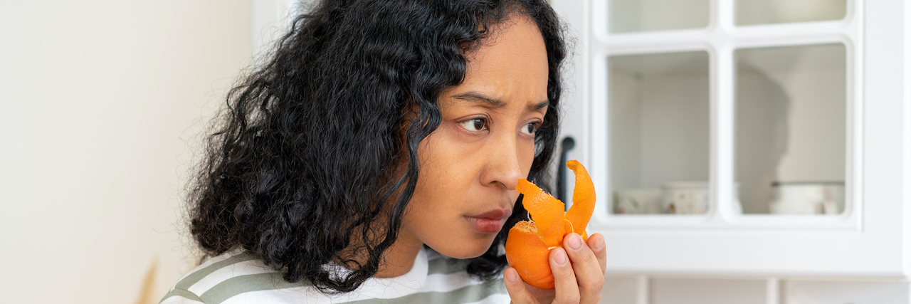 Helping Others Feel Less Alone on Anosmia Awareness Day Woman of color attempting to smell orange rind with concerned look on her face