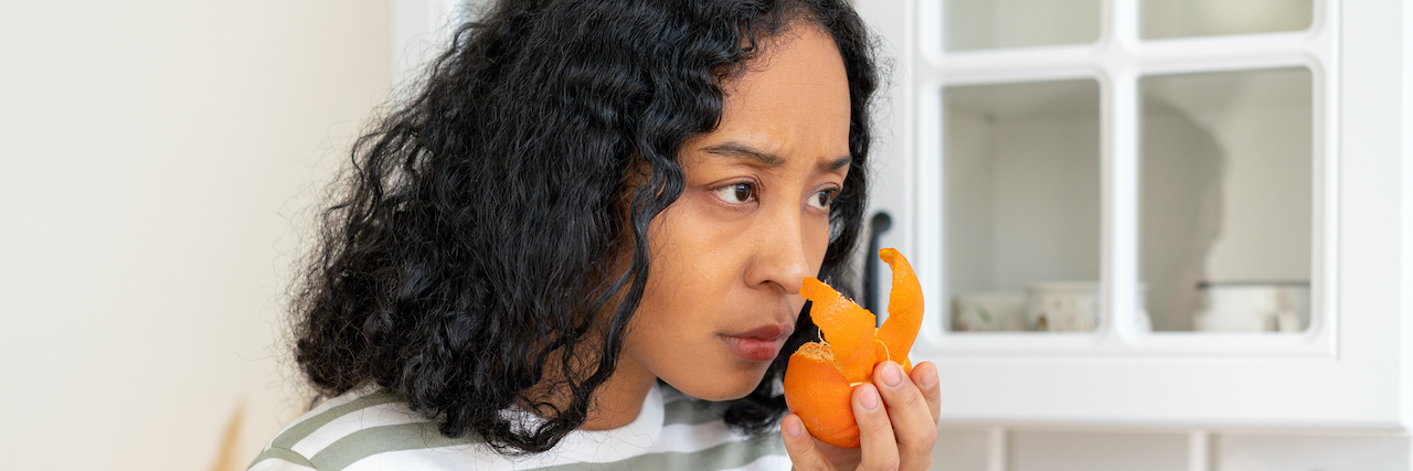 Woman of color attempting to smell orange rind with concerned look on her face