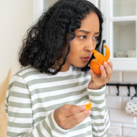 Woman of color attempting to smell orange rind with concerned look on her face