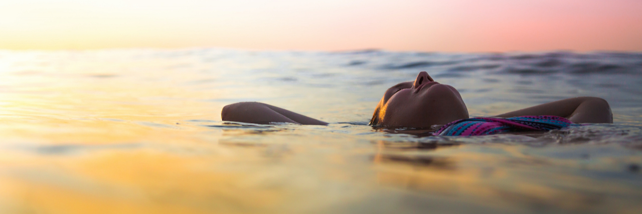 Woman floating in calm water at sunset