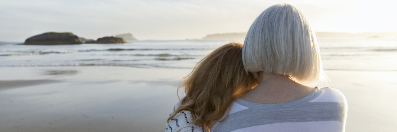 Mother and grown daughter embracing on beach