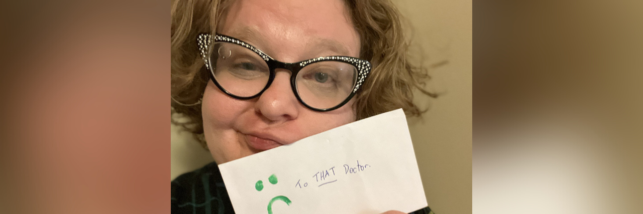 Image of contributor wearing glasses and holding an envelope with the words "To THAT doctor" and a frowny face
