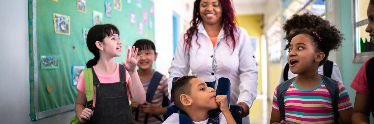 5 Tips for Parents Advocating for Inclusion  Teacher and students walking in corridor at school including student with a disability