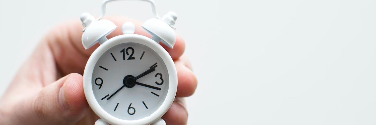 The Alarm Theory I Use to Explain Life With POTS Person's hand holding tiny alarm clock