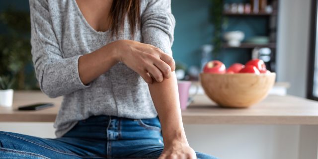 Close-up of woman scratching her arm while sitting on a stool in kitchen