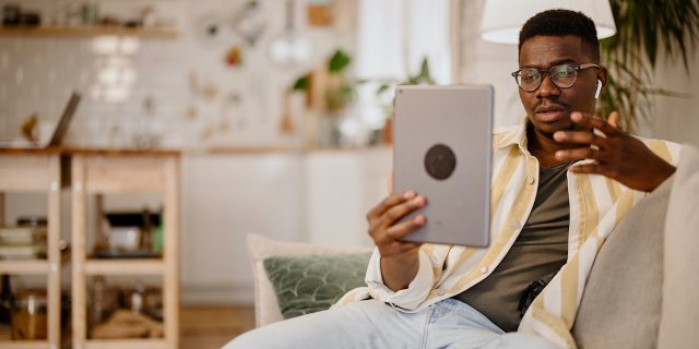 A young Black man at home holding a tablet and speaking