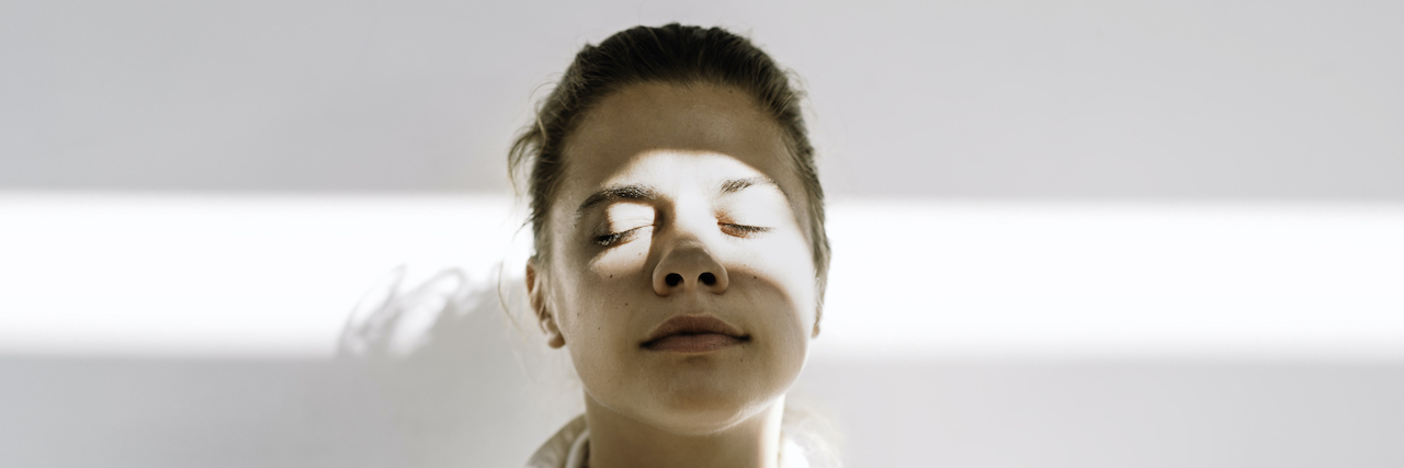 What Is the 3-3-3 Rule for Anxiety and How Does It Work? Person standing against white background, with eyes closed and beam of light across their face