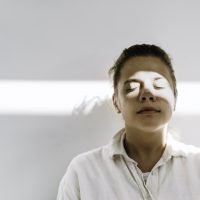 Person standing against white background, with eyes closed and beam of light across their face
