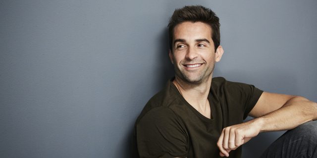 Relaxed man sitting against a wall smiling and looking away