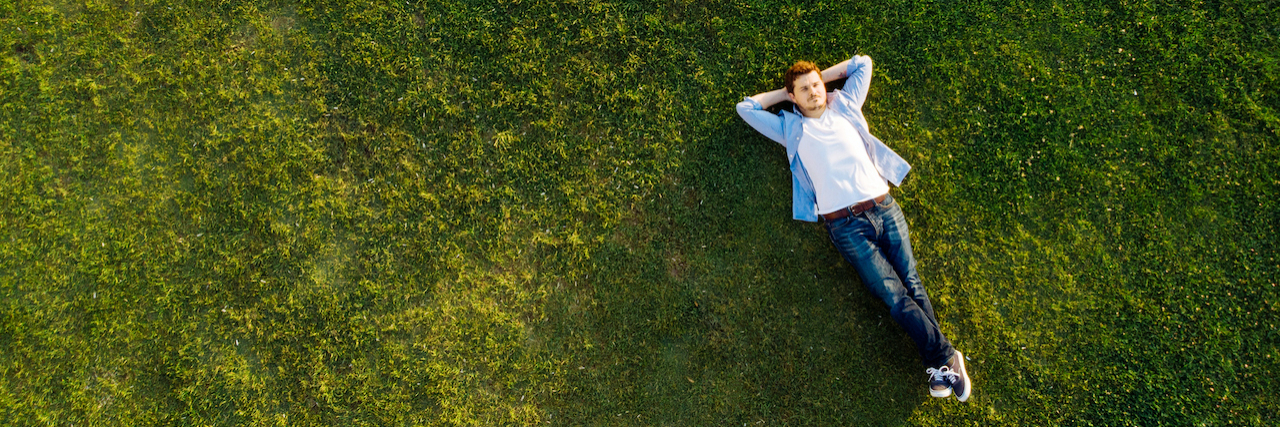Young man laying on grass with arms behind his head