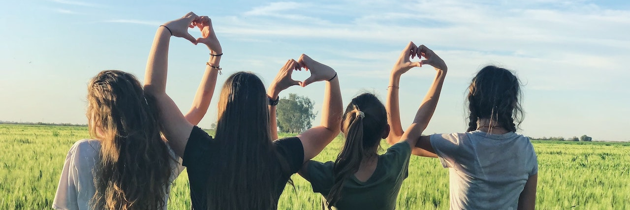 Women forming heart gestures in an open field