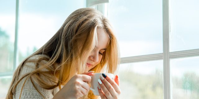 Woman holding a coffee mug sitting next to a window