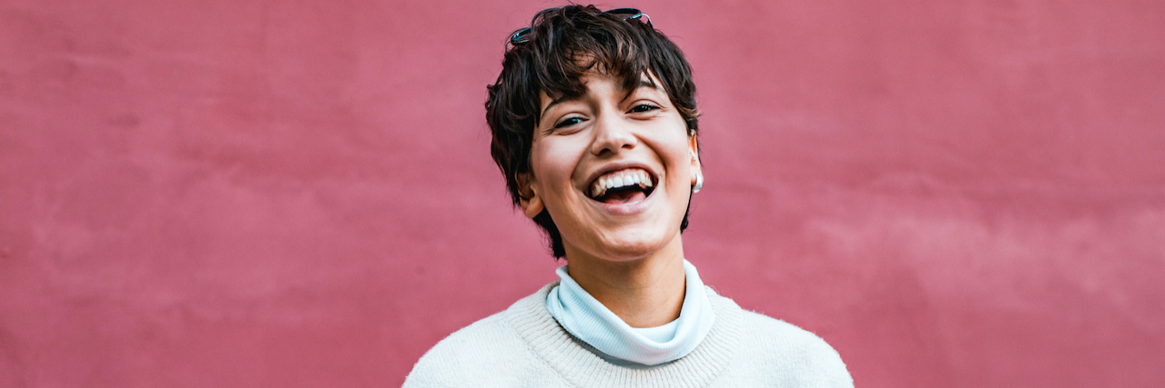 10 Reasons to Recover From an Eating Disorder Woman with short hair smiling in front of red wall