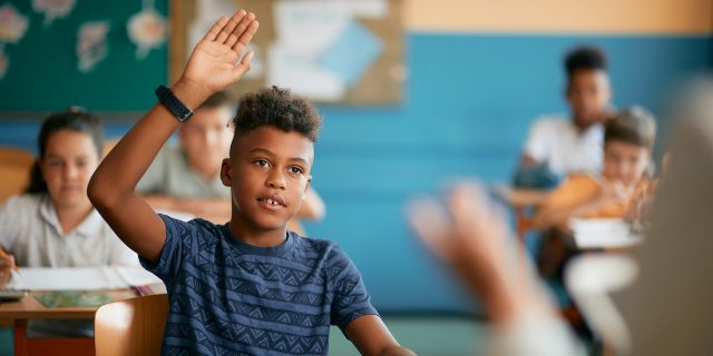 Black elementary student raising his hand in classroom