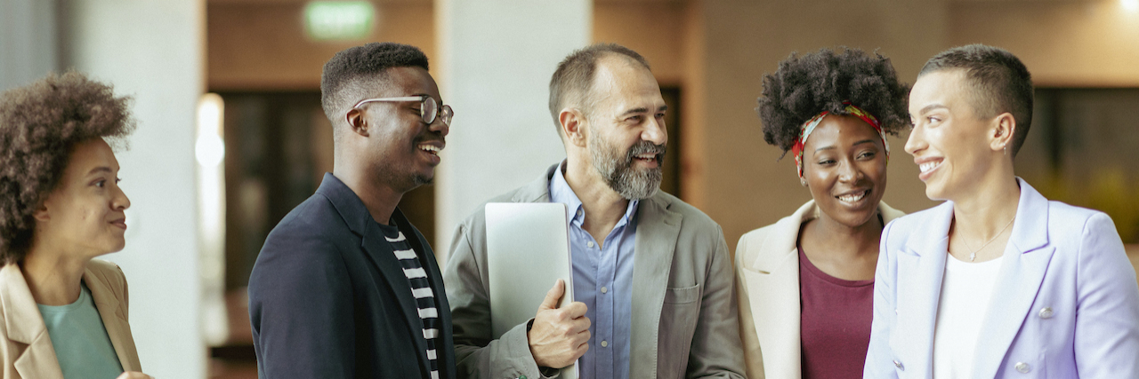 Group of diverse coworkers standing in office and smiling while having an informal conversation