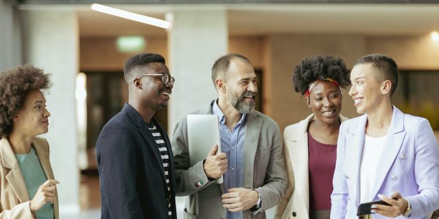 What We Can Do About Underemployment in the Autism Community  Group of diverse coworkers standing in office and smiling while having an informal conversation