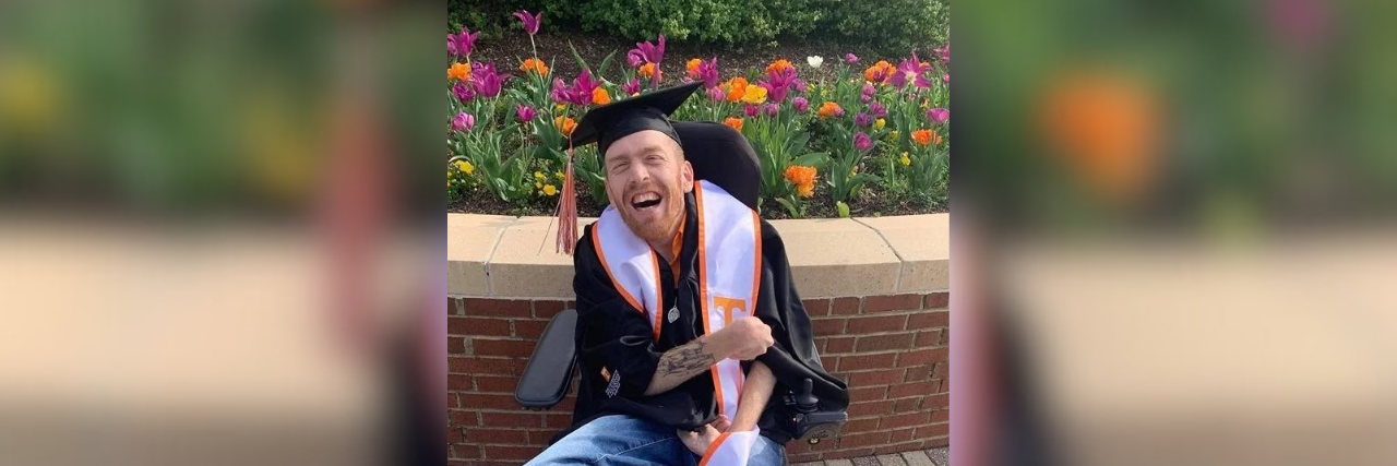 Contributor wearing graduation cap and gown, sitting in wheelchair in front of flowers