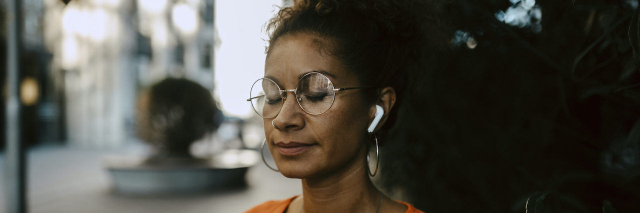 Woman of color with eyes closed wearing ear buds and looking peaceful outside