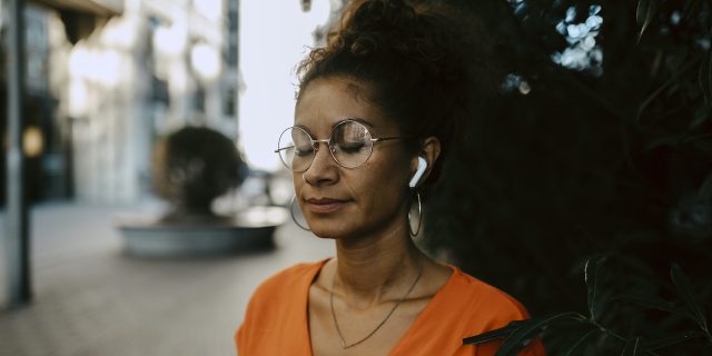 Woman of color with eyes closed wearing ear buds and looking peaceful outside