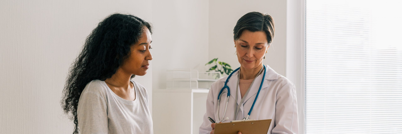 7 Things I Wish I'd Known About Ulcerative Colitis Black woman sitting on examination table and listening to doctor who is holding a clipboard in medical office.