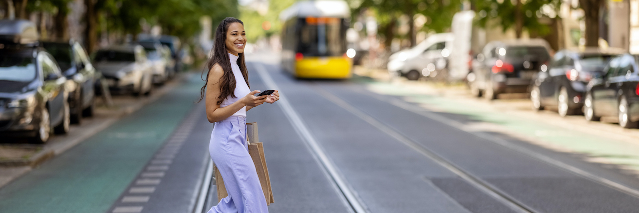 Stylish woman of color, wearing white shirt and purple trousers, crossing a street