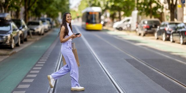 Stylish woman of color, wearing white shirt and purple trousers, crossing a street