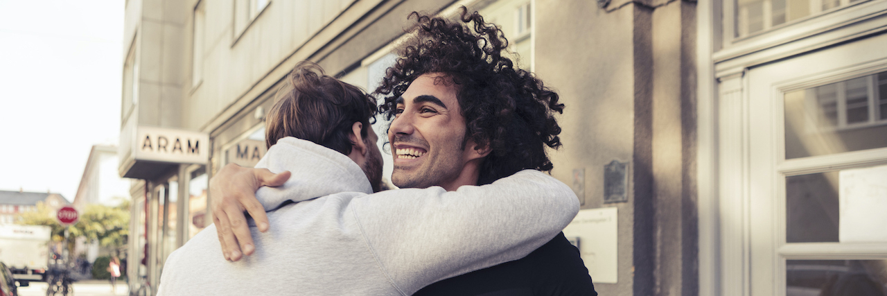 Cheerful male friends hugging each other outside cafe
