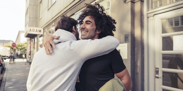 Cheerful male friends hugging each other outside cafe