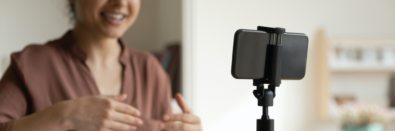 Is TikTok a Valid Self-Diagnosis Tool? Focus on cellphone standing on table on tripod stabilizer, with woman of color in background recording