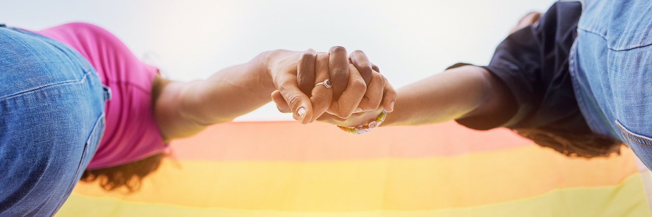 Close up of two women holding hands with gay pride flag above them