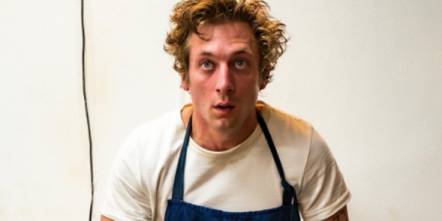 Carmy (actor Jeremy Allen White) from "The Bear" sitting on a counter wearing a blue apron