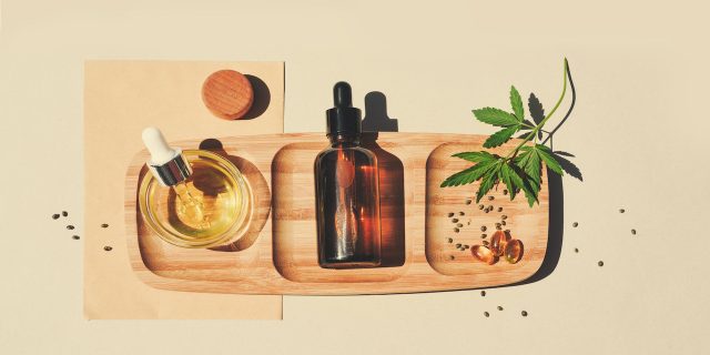 CBD oil, cannabis seeds and leaves on a wooden tray