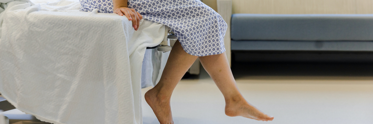 The Diagnostic Turning Point for 5 People With Rheumatoid Arthritis An unrecognizable patient wears a hospital gown and sits on the edge of the hospital bed, dangling their feet.