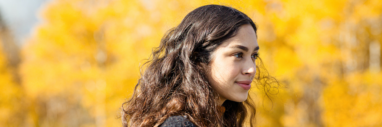 Woman standing outside in front of trees with bright yellow leaves