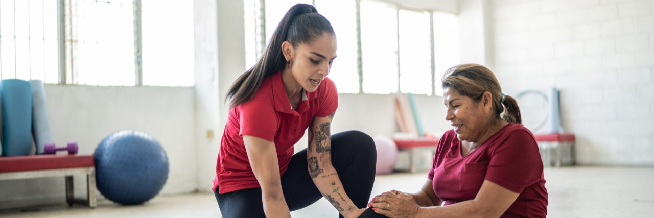 Senior woman being helped by fitness instructor about pain on her knee