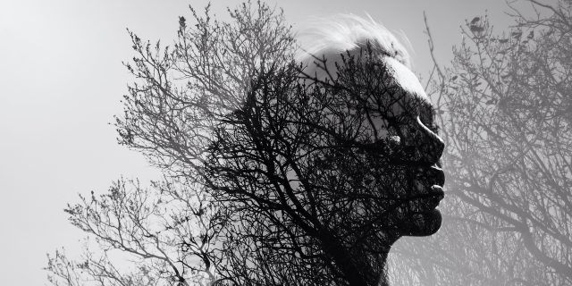 Black and white portrait of a woman in double exposure with a background of bare trees and branches