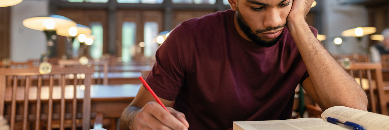 How to Study With ADHD: Comprehensive Tips and Techniques Black man writing in notebook and looking at textbook in library