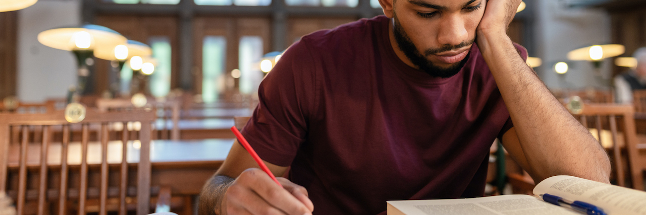 Black man writing in notebook and looking at textbook in library