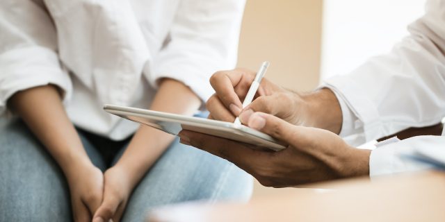 Close up of medical professional writing on tablet with patient next to them