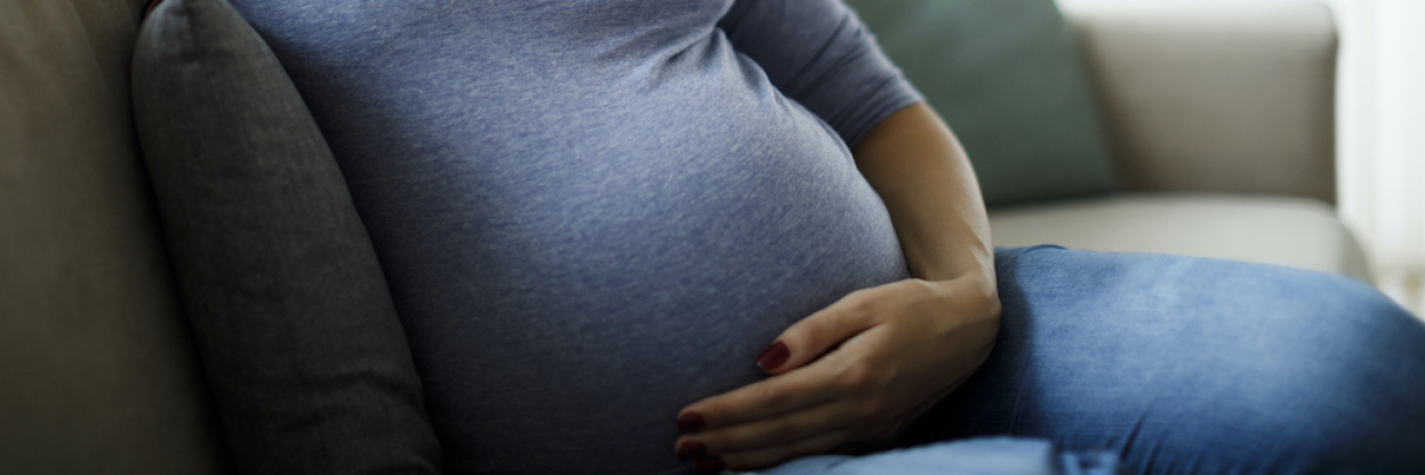 Unraveling Myths: Does an Active Baby in the Womb Mean ADHD? Pregnant woman sitting on couch looking down and holding her belly