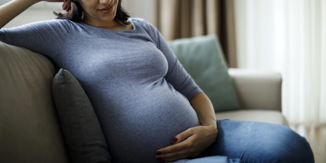 Pregnant woman sitting on couch looking down and holding her belly