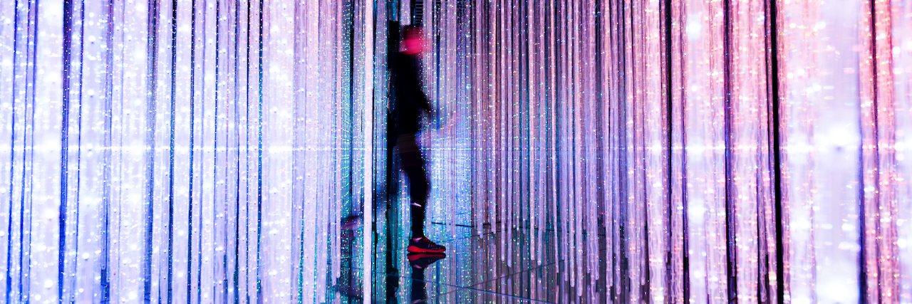 Blurry person walking through colorful, vertical strings of lights