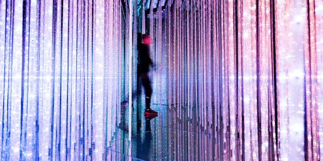 Blurry person walking through colorful, vertical strings of lights