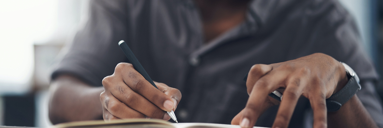 Closeup of a Black man writing in a notebook in an office