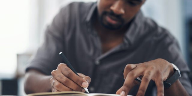 Closeup of a Black man writing in a notebook in an office