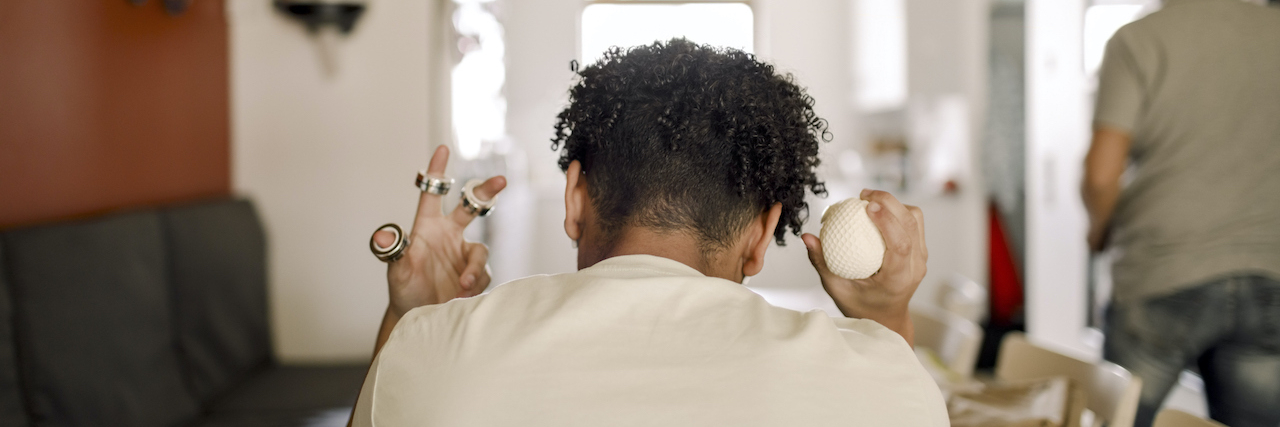 Do People With ADHD Stim? Rear view of person sitting at table at home holding ring fidgets on fingers and stress ball in other hand