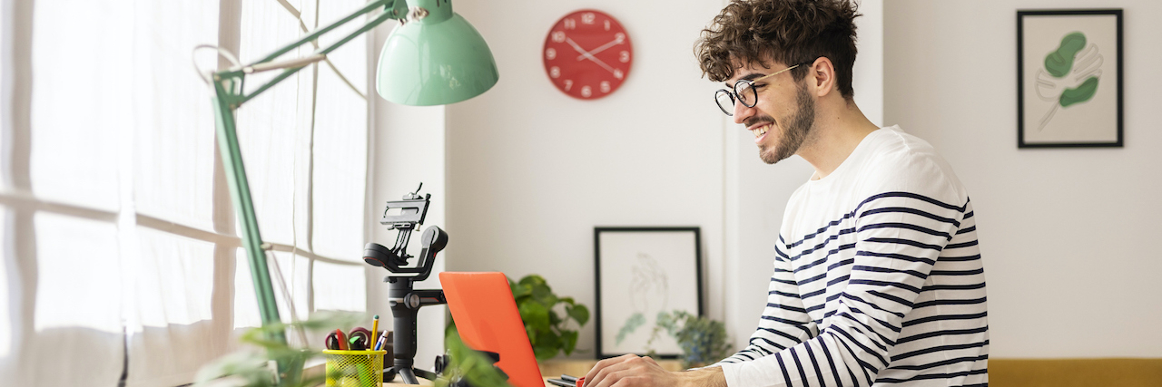 Strategies for Success: How to Be Productive With ADHD Young man smiling while working on laptop and sitting at desk