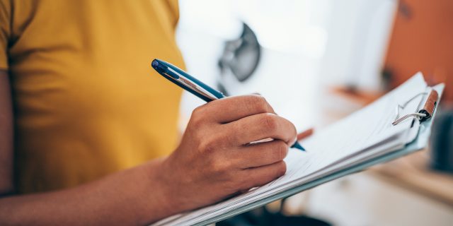 Cropped shot of an woman's hand making notes on a clipboard in an office